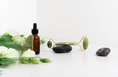 Yüz masajı için Jade Roller. Yeşil gua sha mermer beyaz arka planda düz yatıyordu. Yaş, kaldırma ve tonlama tedavisi, akupres. Eustoma çiçekleri. Pipetli serum kahverengi şişe..