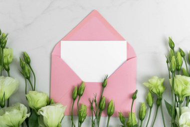 Gerçek fotoğraf. Pembe zarf kare davetiye modeli ve Eustoma çiçekleri. Üst görünümü kopyalama alanı, açık gri mermer arkaplan. Markalaşma ve reklam şablonu.