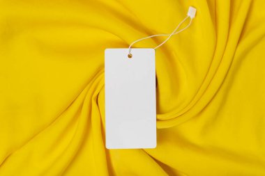 Beyaz giysi etiketi, kurdeleli boş model şablonu, tasarımınızı yerleştirmek için. Premium pamuk sarısı kumaş arkaplanda.