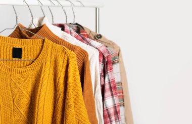 Sonbahar modası kıyafetleri askılarda asılı duruyor. Bej rengi trençkot, kazaklar, ekose gömlekler. Uzay düzeni, kış temizliği. Model, şablon.