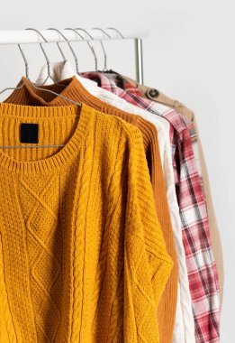 Sonbahar modası kıyafetleri askılarda asılı duruyor. Bej rengi trençkot, kazaklar, ekose gömlekler. Uzay düzeni, kış temizliği. Model, şablon.