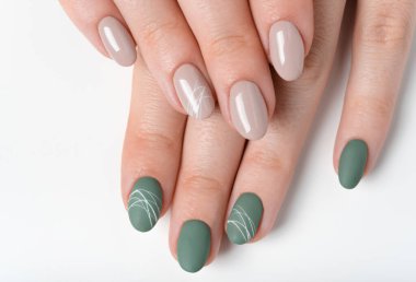 Yeşil zeytin rengi tırnakları ve beyaz arka planda bej renkli tırnakları olan genç bir kadının elleri. Farklı renkte tırnaklar. Manikür, güzellik salonu. Metin veya logo için boşluk kopyala. soyut