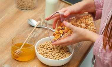 Kadın elleri hızlı bir kahvaltı hazırlar. Yuvarlak mısır gevreği topları, tatlım. Mutfakta süt. Fındık, badem ve fındık.