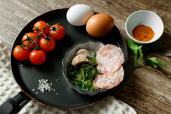 Összetevők serpenyőben sült tojáshoz: tojás, gyógynövények, fokhagyma, cseresznye paradicsom, paprika, só és kolbász — Stock Fotó