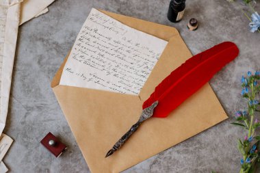 Kağıt mektuplar, el halısı, tüy kalem, mürekkep hokkası ve çiçekler masanın üzerinde. Parlak güneşli bir gün. Yukarıdan görüntüle.