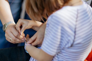 Anne küçük kızının kolundaki saati takmasına yardım ediyor.