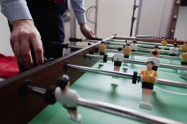 Ofisteki bir adam masa futbolu oynuyor. Sarı beyaz üniformalı küçük oyuncaklar.