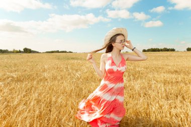 Sarı buğday tarlasında parlak kırmızı elbiseli kız, güneşli bir gün, mavi gökyüzü.
