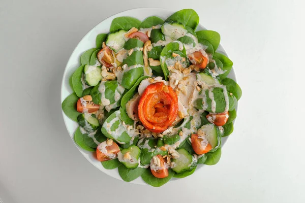 Healthy greens salad with tomato, spinach and nuts on a white plate on a white plate — Stock Photo, Image