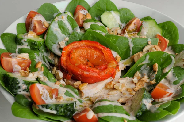 Healthy greens salad with tomato, spinach and nuts on a white plate on a white plate — Stock Photo, Image