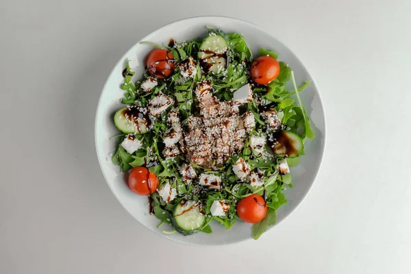 Healthy greens salad on a white plate on a white plate with balsamic sauce, sesame seeds, chicken and arugula — Stock Photo, Image