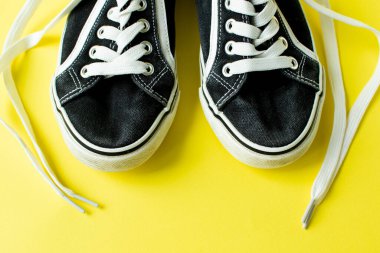 Sarı arka planda eski siyah ayakkabılar, çözülmüş bağcıklar.