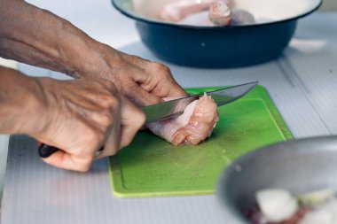 Yaşlı kadınların elleri bıçak tutar, tavuk budu doğrarlar yeşil kesme tahtasında yemek için.