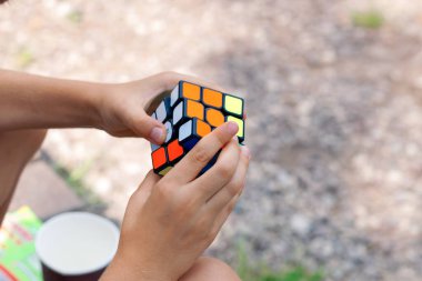 Bir çocuk elinde bir Rubiks küp yapbozu tutuyor ve doğada topluyor, bir çocuğun ellerine yakın plan.