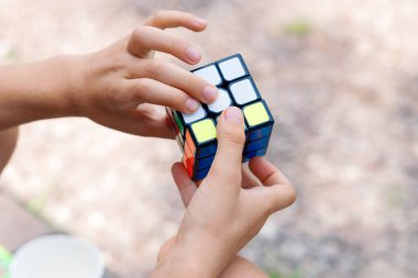 Bir çocuk elinde bir Rubiks küp yapbozu tutuyor ve doğada topluyor, bir çocuğun ellerine yakın plan.