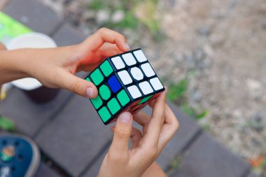 Bir çocuk elinde bir Rubiks küp yapbozu tutuyor ve doğada topluyor, bir çocuğun ellerine yakın plan.