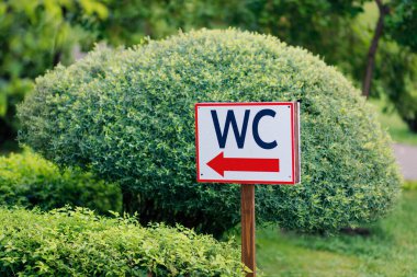 Yeşil güzel bir parktaki tuvaleti işaret eden büyük parlak bir tabela.