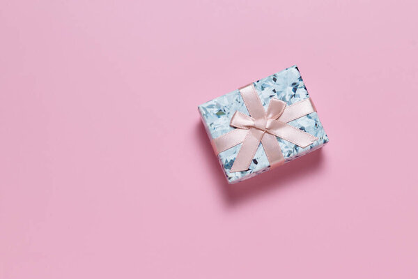 Small gift box with pink ribbon bow on pink background