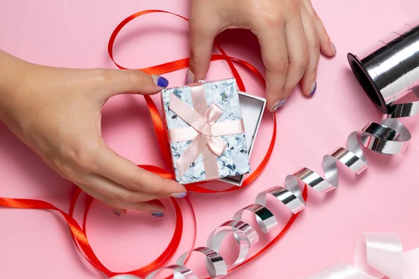 Zbliżenie dłoni trzymającej małe pudełko z kokardką na solidnym różowym tle, w którym znajdują się wstążki do pakowania — Zdjęcie stockowe