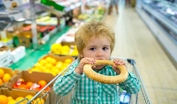 Un mignon petit garçon mange un chignon au supermarché. Snack pour un enfant lors du shopping. — Photo