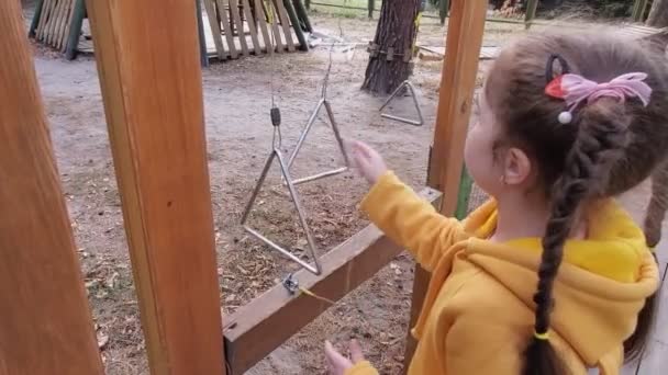 Menina bonito em uma camisola amarela jogando triangolo em um parque infantil ao ar livre no parque da cidade de outono. — Vídeo de Stock