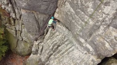 Kaya tırmanışçısı, kireçtaşı bir kayaya halat ve kancayla tırmanır. Açık havada aktif yaşam tarzı ve kaya tırmanışı konsepti. Kuş bakışı bir kayanın ve sonbahar ormanının güzel manzarası..