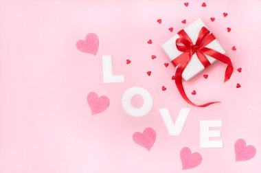 Sevgililer Günü kompozisyonu, hediye kutusu ve beyaz harflerle yazılmış kağıt kelimelerle aşk, pembe arka planda keçe ve şeker kalplerle. Tatil kartı konsepti