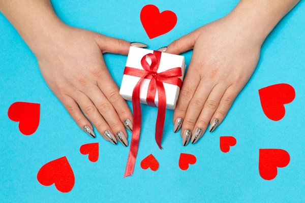 Kırmızı ya da pembe kurdeleli, açık mavi arka planda kağıt kırmızı kalpli bir kadının elleri. Doğum günü, Sevgililer Günü, Noel, Yeni Yıl arkaplanı. Düz yatıyordu