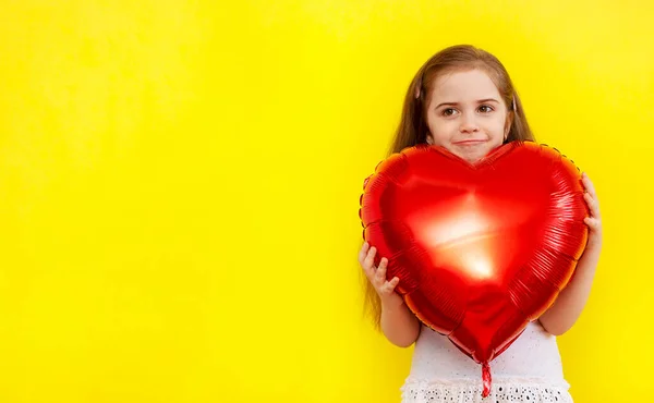 Sarı arka planda kocaman kırmızı bir kalp şeklinde balon tutan mutlu küçük kız. Bahar, Kadınlar Günü, Sevgililer Günü, Doğum günü, Anneler Günü konsepti. Kopyalama alanı.