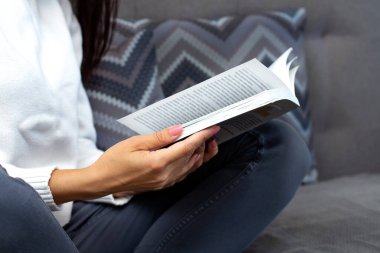 Kitap okuyan genç bir kadın, yakın plan, evin iç mimarisi. Kız öğrenci eğitimlidir. Evde kal konsepti.