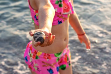 Pembe mayolu bir kız elinde güzel bir deniz taşını tutuyor yaz denizinin arka planında