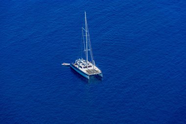 Mavi denizin arka planında beyaz yelkenli katamaran.