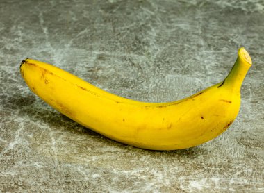Sarı, olgun, soyulmamış, gri bir arka planda muz. Yakın plan..