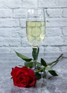 Bir bardak beyaz şarap ve kırmızı bir gül. Işık arkaplanına yakın plan.