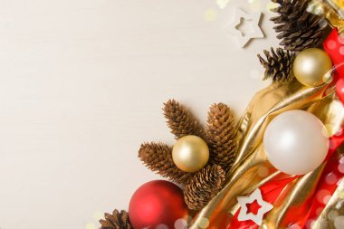 Noel süsleri ahşap beyaz bir masanın üzerinde yatar. Noel topları, çam kozalakları, altın bez, yıldızlar, kırmızı kurdele. Üst görünüm, metin için yer. Bir tebrik kartı için kutlama planına ihtiyacım var. Kopyalama alanı