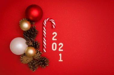 Yılbaşı topları, çam kozalakları, şeker kamışı ve 2021 numaralarıyla kırmızı arka planda mesajlaşma yeri olan bir Noel modeli. Yukarıdan bak. Yatay format. Kopyalama alanı