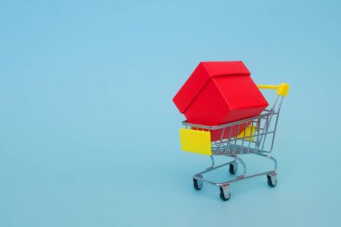 Kırmızı bir hediye kutusu mavi arka planda sarı saplı bir market arabasında yatıyor. Yan görüş. Metin için yer.