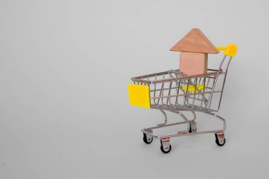 Gri bir arka planda, market arabasındaki ahşap yapı taşlarından yapılmış doğaçlama bir ev. Yan görüş. Yatay format. Metin için yer.