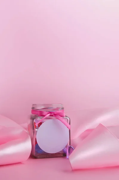 ロゴの場所とモックアップ ピンクの背景にハートの入ったガラス瓶とピンクのシルクリボン バレンタインデーのコンセプト テンプレート バナー テキストの場所 — ストック写真