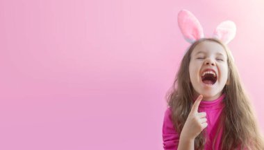 Tavşan kulaklı neşeli kız pembe arka planda kahkahalarla gülüyor. Paskalya tatiline hazırlanıyorum. Pankart. Yatay format. Mutlu çocukluk kavramı. Kopyalama alanı