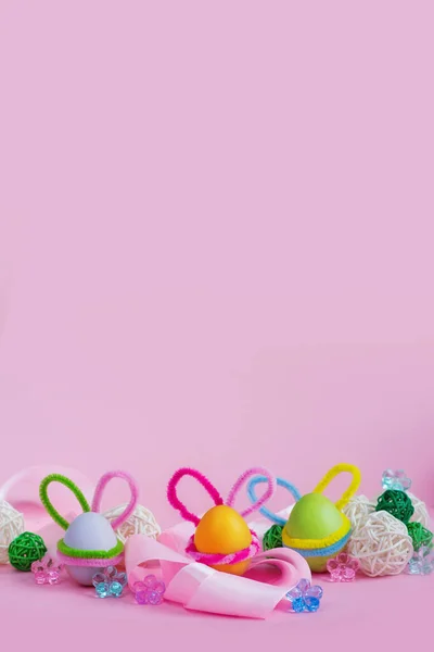 イースターバニーの耳を持つカラフルな卵のセットは ピンクの背景にリボンや装飾品の近くにあります 縦のバナー イースター休暇のためのポストカード テキストの場所 — ストック写真