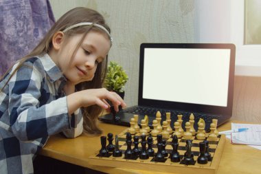 Çocuklar için çevrimiçi satranç kursları. Küçük kız internette satranç oynuyor. Satranç tahtası ve dizüstü bilgisayarı olan bir Hild. Beynin gelişimi için oyunlar ve karantinada kullanışlı zaman.