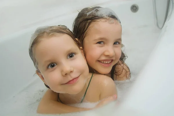 Barnhygien. Två underbara barn badar tillsammans i badrummet. Lekfulla tjejer tittar upp ur badet och ler mot kameran. Barnhygien. — Stockfoto