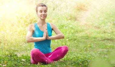Lotus pozisyonunda oturan güzel genç bir kadın, kolları bağlı, zen jestleri yapıyor. Yoga açık havada. Sağlıklı yaşam tarzı ve rahatlama konsepti. Metin için yer
