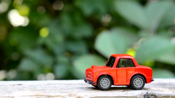 Malé dětské ručičky kutálí červené autíčko na dřevěné desce v parku venku. Copyspace — Stock video
