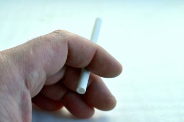 Gri arka planda bir sigarayla el.