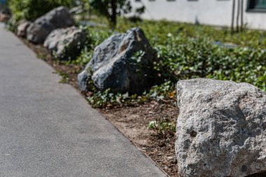 Güneşli bir günde asfalt yaya bölgesi boyunca süs olarak büyük taşlar bulunur. ön plana odaklan, arkaplan bulanıklaştı