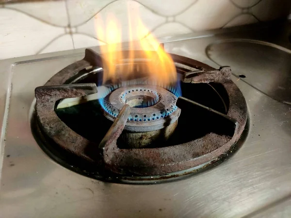 Mutfak arka planında yanan mavi ve sarı gaz sobası. Ocakta gaz ocağı var.