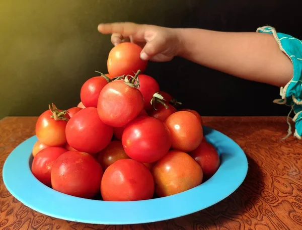Pflanzliche Tomate in Teller von Kinderhand auf strukturiertem Holzhintergrund mit Platz für Text angeordnet. — Stockfoto