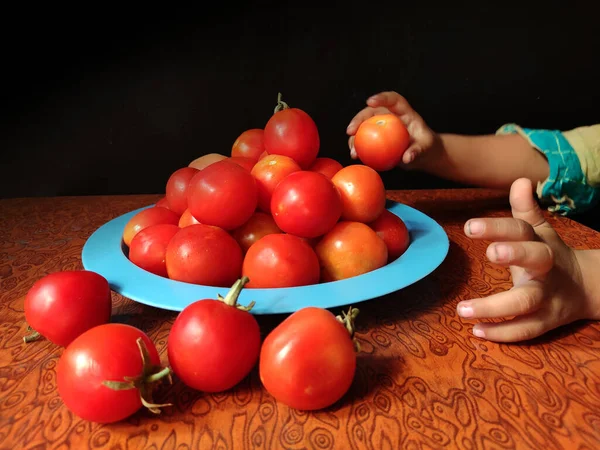 Pflanzliche Tomate in Teller von Kinderhand auf strukturiertem Holzhintergrund mit Platz für Text angeordnet. — Stockfoto